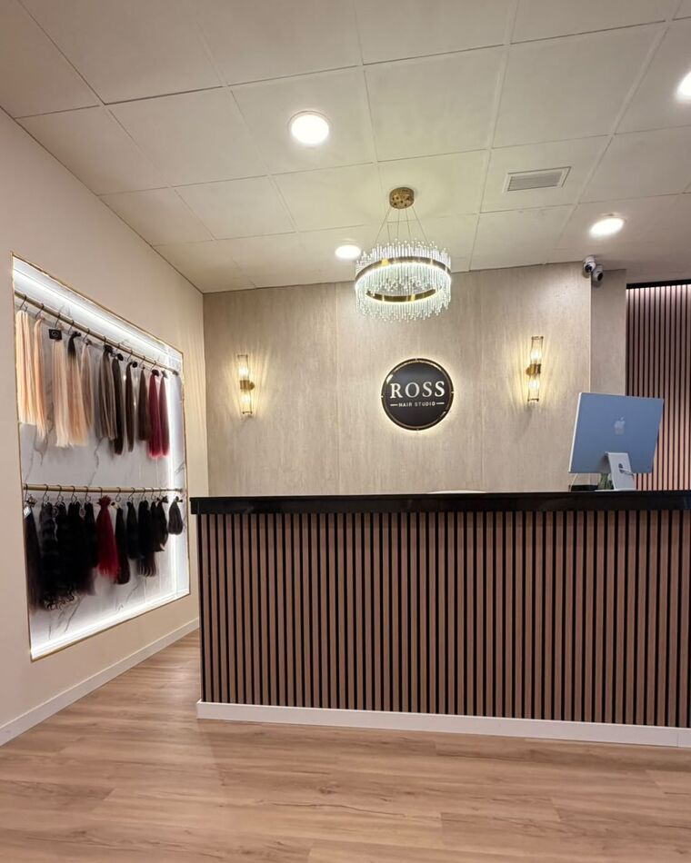 Recepción de Ross Hair Studio con el muro iluminado de extensiones, la lámpara de cristal y el logo en la pared