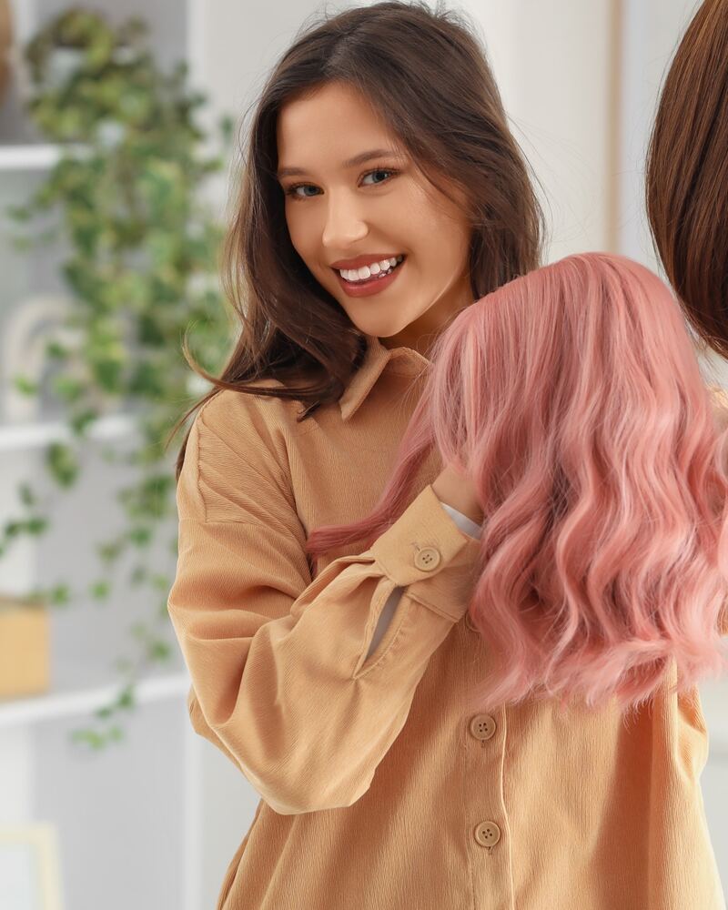 Mujer sonriente eligiendo entre una peluca castaña y otra rosa