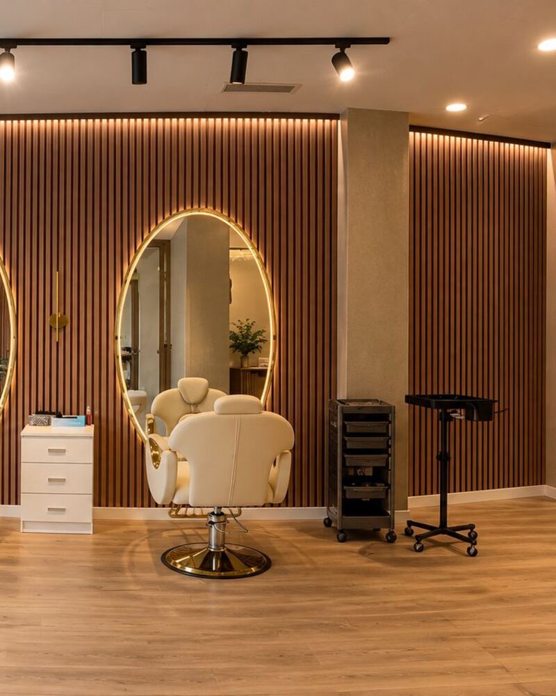 Interior de Ross Hair Studio en Patraix: pared de lamas de madera, espejos ovalados con luz dorada y sillones color crema