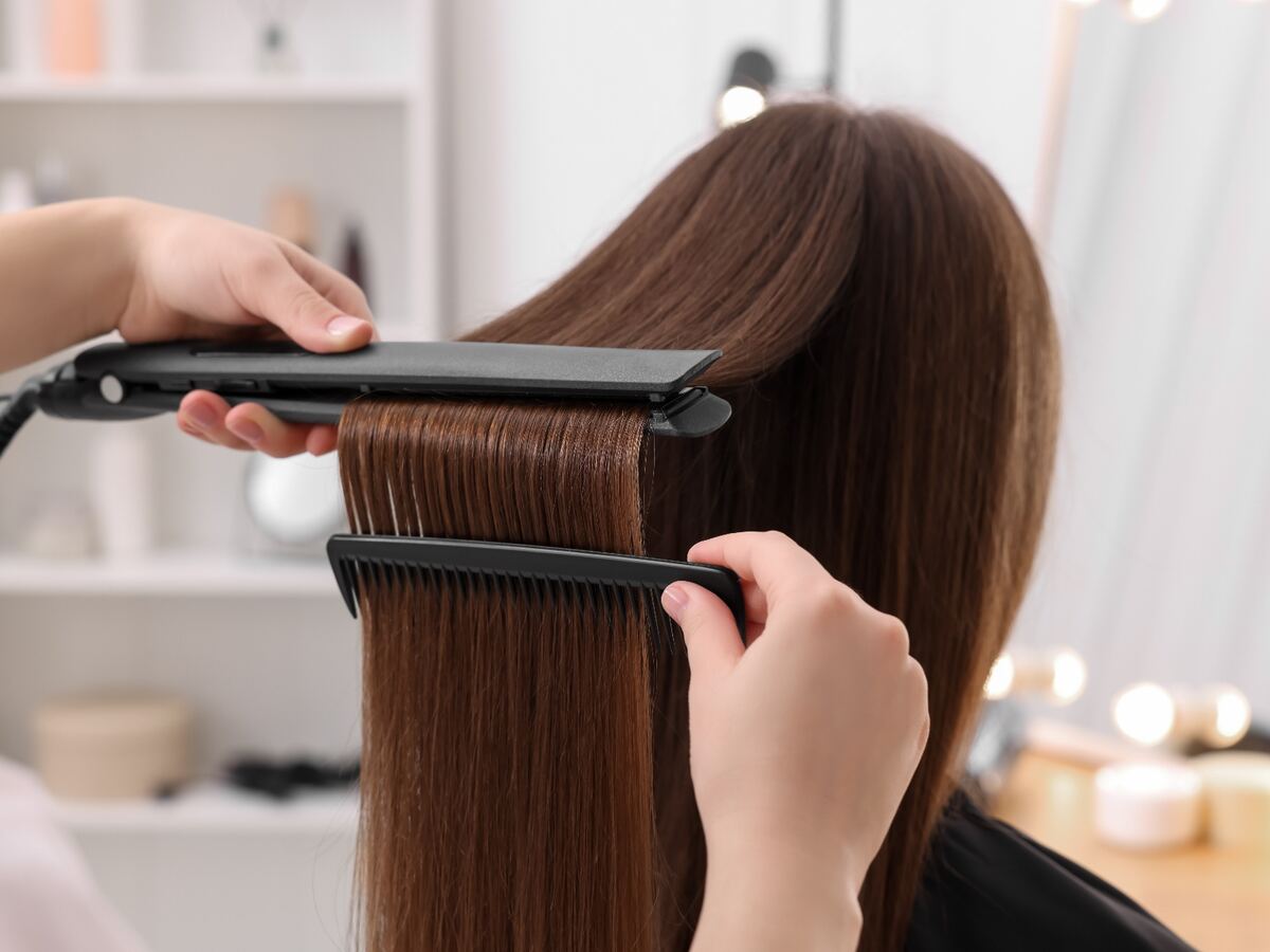 Peluquera alisando con plancha una melena castaña larga en el salón