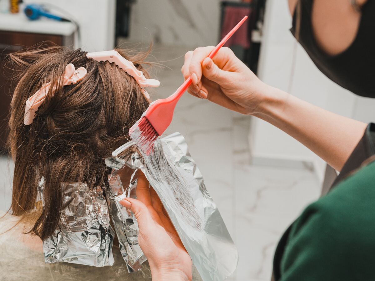 Peluquera pintando mechas con pincel sobre el pelo de una clienta