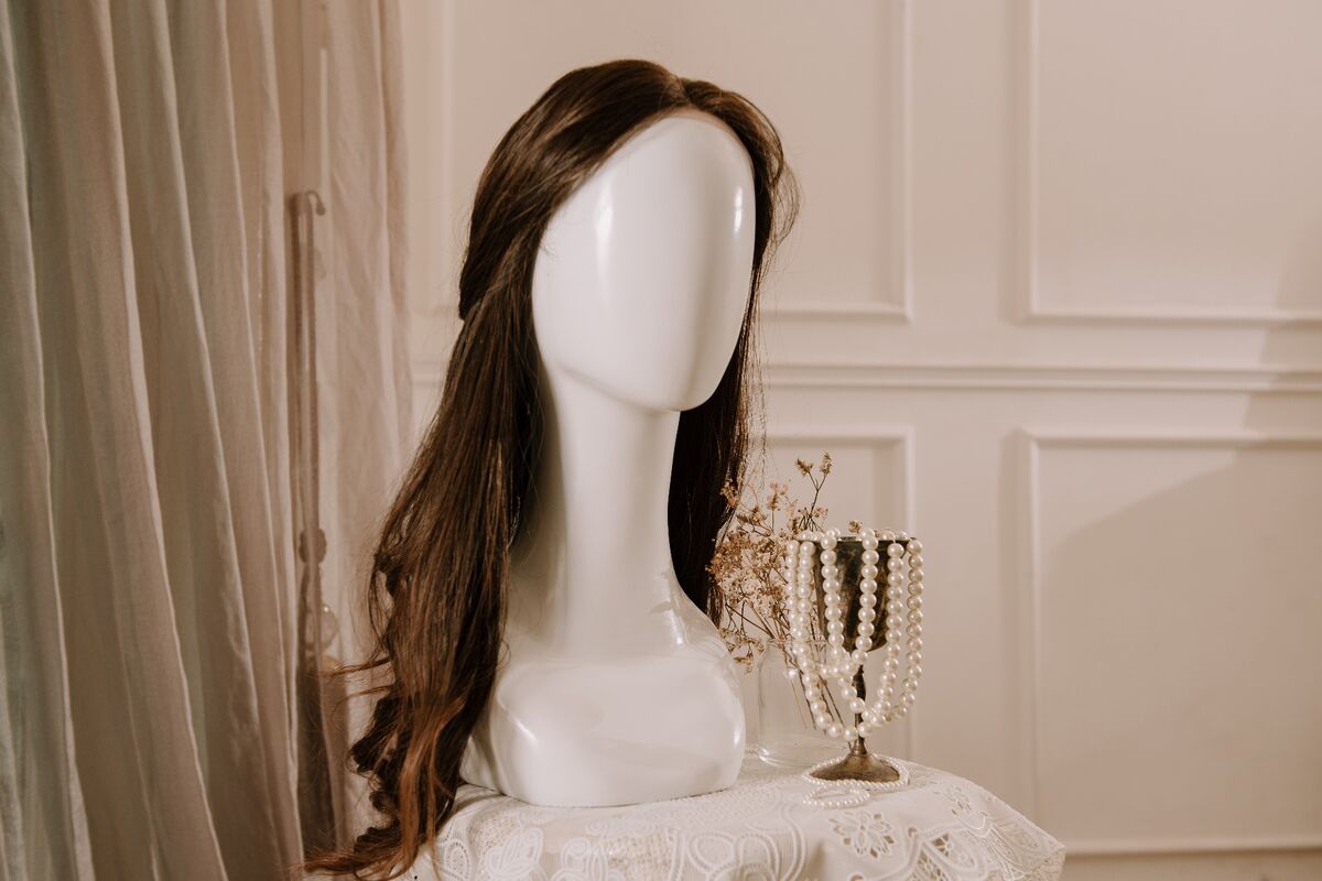 Peluca castaña larga sobre una cabeza de maniquí junto a un collar de perlas